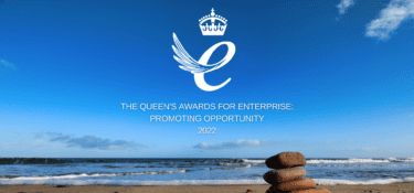 Queens award logo against a photo of a pile of stones stacked on a sandy beach as the tide rolls in. Text reads: The Queens awards for enterprise. Promoting opportunity 2022.
