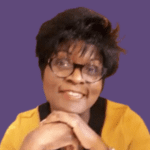 Profile picture of Ermine Benjamin, smiling at camera, wearing yellow, with hands together under chin.