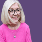 Image of Lynda Freeman smiling, wearing a pink jumper and black glasses.