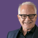 Image of Thomas Imfeld smiling at the camera, wearing a black blazer, shirt and glasses.