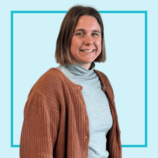 Light blue background with image of Alienor Falconer smiling at the camera and wearing a blue turtle neck and brown cardigan.