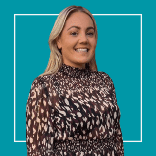 Holly Garland, stood against a teal background, smiling at the camera and weathering a brown leopard print dress.