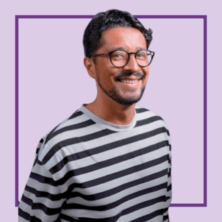 Light purple background with image of Zaq Mughal wearing a stripey black and white top and glasses, smiling at the camera.