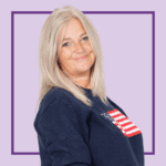 Light purple background with image of Annie Clark smiling at the camera, wearing a navy blue jumper with the US flag on