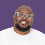 Tumi Sotire, smiling at the camera wearing glasses and a white jumper, against a purple background